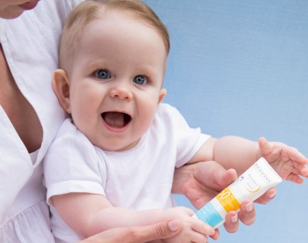 Baby with a spray bottle of mineral sunscreen, SPF50+.